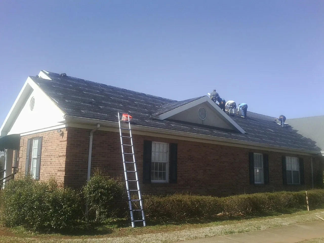 Crew tearing shingles off a brick ranch roof with a ladder set — Emergency Roof Repair work by our crew in Marion