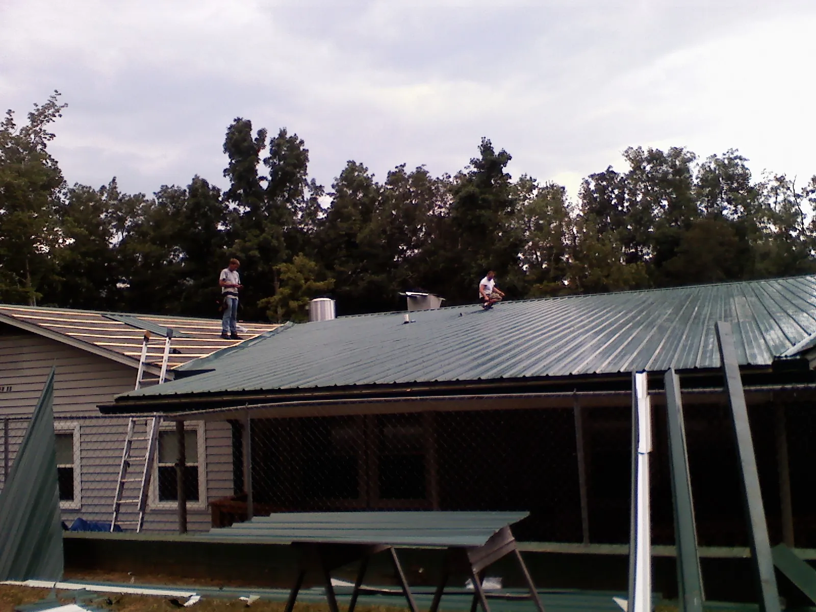 Two roofers installing green metal panels above a covered porch in Marion